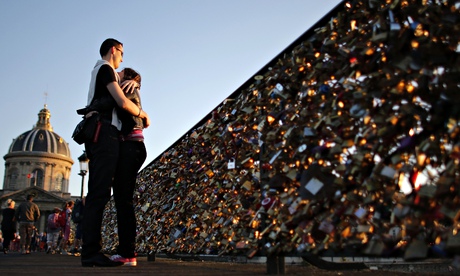 A couple embraces on Paris's Pont des Arts with its fence covered with padlocks