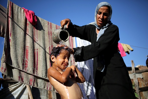 A Palestinian mother Na-eema Abu Shaweesh washes her 4-year-old daughter Sara in her home of tents. The family of 14 are one of many who live in tents in the east of Gaza City