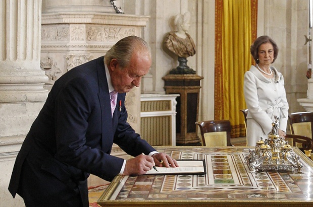 Spain's King Juan Carlos signs an abdication law in the presence of Queen Sofia during a ceremony at the Royal Palace in Madrid, Spain, on Wednesday