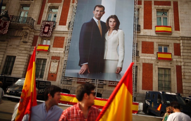 People holding Spanish flags walk past a poster showing Spain's new King Felipe VI and his wife Queen Letizia in Madrid.
