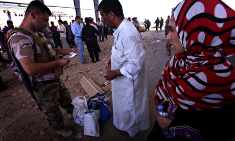 An Iraqi Kurdish security guard checks the ID cards of families fleeing violence in Mosul