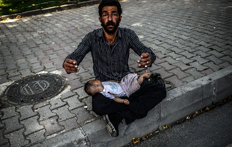 20 Photos: A Syrian refugee with a baby on his lap begs in an Istanbul street