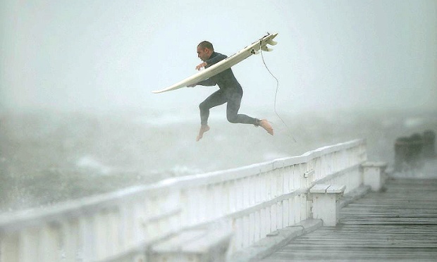 Ένα surfer πηδά από την αποβάθρα στο Port Phillip Bay για να επωφεληθούν από τα κύματα σαν μια καταιγίδα βλεφαρίδες την περιοχή Μελβούρνη, Αυστραλία