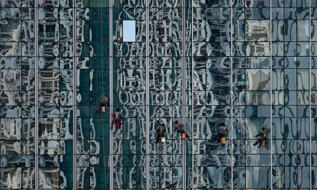 Οι εργαζόμενοι τον καθαρισμό γυάλινο τοίχο ενός κτιρίου που φέρει μια αντανάκλαση των άλλων κτιρίων στην οικονομική περιοχή στο Πεκίνο