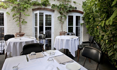 Tables at Toto's with tablecloths outside a building with ivy 