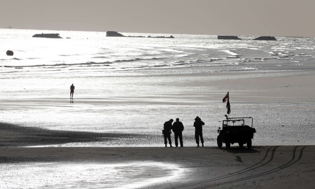 Men dressed in vintage World War II US military uniforms stand next to a Willis jeep, on the beach, in the morning in Arromanches, western France.
