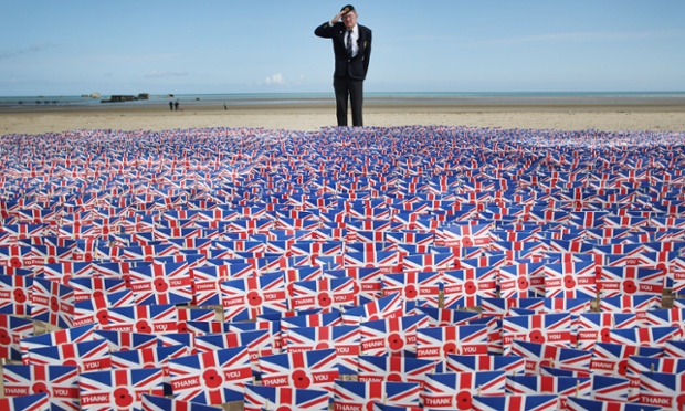 WW2 veteran Fred Holborn, from the Fleet Air Arm, salutes as he looks at British Legion Union flags carrying thank you messages planted in the sand on Gold beach.