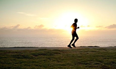 A silhouette of a jogger running alone with sun on horizon