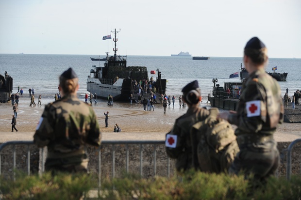 People walk on the beach along WWII ships prior to the start of a joint French-Dutch D-Day commemoration ceremony in Arromanches, Normandy.