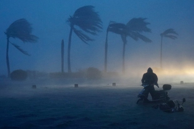 Battered by the elements: a man pushes his scooter along a flooded seaside street as Typhoon Rammasun hits Haikou in China.