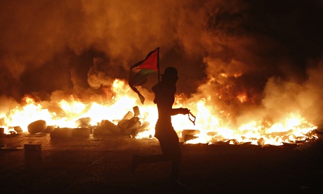 A protester holds a Palestinian flag at a barricade of burning tyres in clashes with Israeli troops