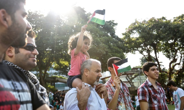 Singapore: A girl sits on her father's shoulders waving a Palestinian flag at a protest in Hong Lim Park