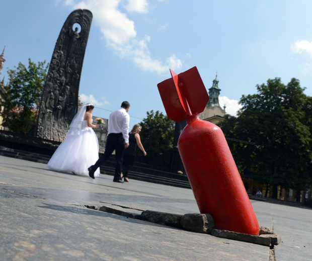 A just married couple walks past an art installation showing an unexploded bomb, set near the Taras Shevchenko monument (L) in the center of the western Ukrainian city of Lviv, close to Poland's border on July 31, 2014. Through the installation, the Lviv-based NGO Varta-1 aims at raising residents' awareness about the current conflict taking place in the country, some 1200 kilometers away far east, and collecting funds, equipment and medicine for Ukraine's Army soldiers needs.