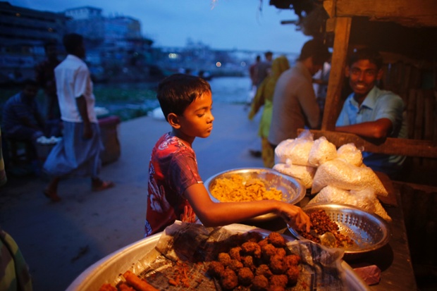 A boy sells food by the river Buriganga in the evening in Dhaka