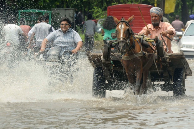 Looking more like a river than a road, Indian commuters make their way along a flooded street after a heavy downpour in Amritsar.