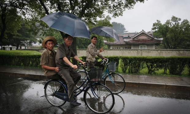 North Korean men cycle in the rain past homes built for farmers at the Mangyongdae Cooperative Farm