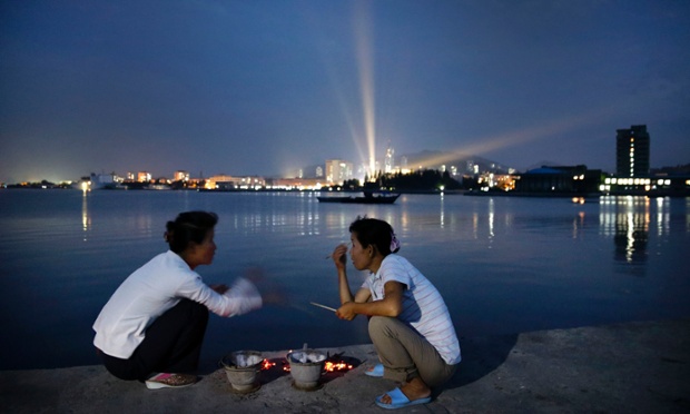 North Korean women talk over pots of burning charcoal for cooking seafood on a pier leading to Jangdok Island at dusk