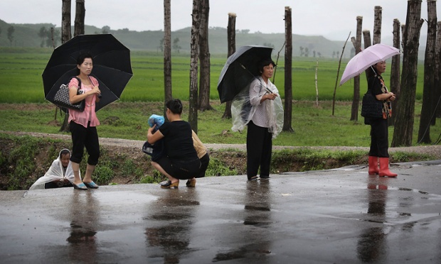 North Koreans shelter themselves from the rain as they wait for transportation along the road, Saturday, July 26, 2014 in the North Pyongan Province, North Korea.