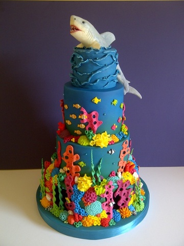 'Shark Reef Cake: This cake took FOREVER to complete! 30+ hours. BUT I had an idea and I just had to keep going until it was complete. I could have made life a lot easier for myself if I'd just made a shark topper, but noooo, I had to make him swimming through the top tier, didn't I? The bottom tier was polystyrene into which I carved 'underwater' caves and then back lit them with blue lights recessed into the board. I loved making it, but OMG it was such a labour of love!'