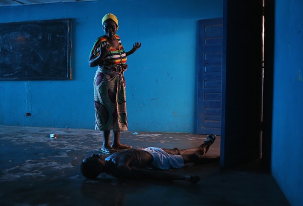 Umu Fambulle stands over her husband Ibrahim after he staggered and fell, knocking himself unconscious in an Ebola ward in Monrovia, Liberia.
