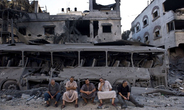 Five Palestinian men sit on August 20, 2014 next to a destroyed bus and houses in front of a house that was completely demolished after it was targeted by Israeli airstrikes late on August 19. Hamas said on August 20 that an Israeli air strike killed the wife and child of its Gaza military chief, as a temporary ceasefire went up in smoke and Cairo truce talks froze.