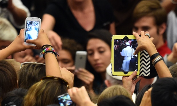 People take pictures of Pope Francis saluting the crowd before his general audience in the Paul VI hall at the Vatican