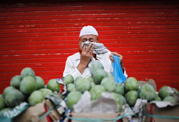 A vendor sneezes while selling mangoes along a roadside in the old quarters of Delhi