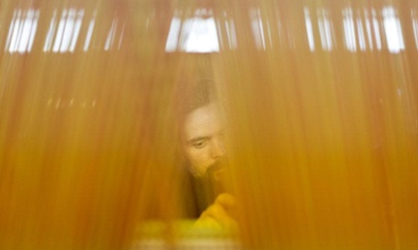 G.B. England. Bradford.  A worker seen through the criss-crossing threadwork of a weaving machine. William Halstead, weavers of fine mohair and worsteds, operating since 1875. 2013.