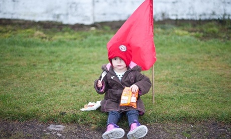 little girl eating crisps sitting on the grass in front of a flag