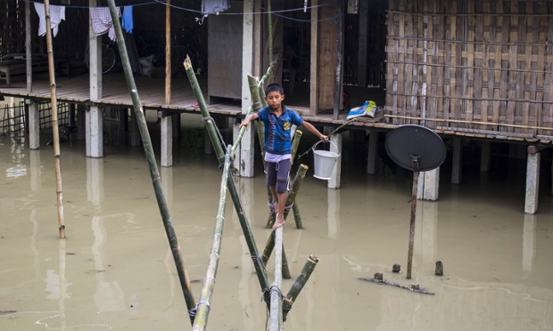 A tribal boy walks through a makeshift bamboo bridge to collect drinking water as his house is submerged in flood-waters at Dikhowmukh in Sivasagar district in Assam, India