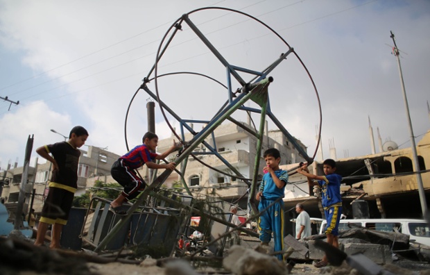 Palestinian children play around a destroyed mini ferris wheel near the remains of homes that were destroyed by an Israeli air strike on Rafah town in the southern Gaza Strip