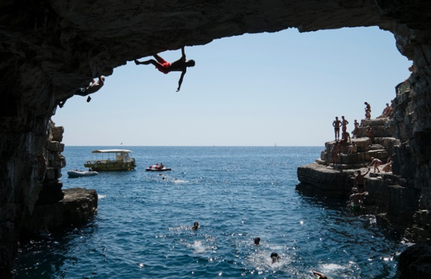 Two young men climb  in an 8 to 10 meter-high cave of Stoja on August 4, 2014 near Pula, Croatia. Deep Water Soloing (DWS), free climbing over water, is a relatively new discipline and is popular with climbers wanting to go rock climbing during the high summer temperatures. Climbing over deep water means most of the climbing routes are safe for beginners but still offer a challenge for the more advanced climber. There are many opportunities for DWS at the mile-long cliffs of Croatia.