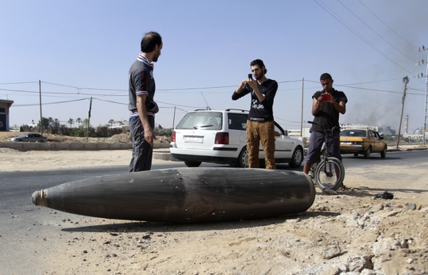 Palestinian men pose for photographs beside an unexploded Israeli shell on a road in Deir al-Balah.