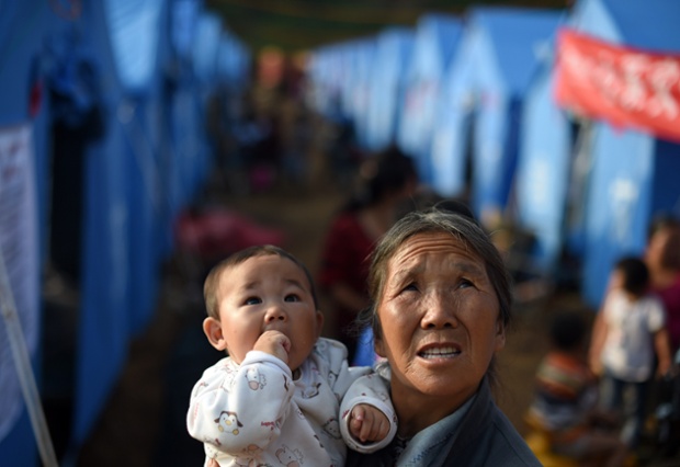 A woman and child watch a helicopter land near rows of tents housing earthquake survivors at Longtoushan, in China's Yunnan province