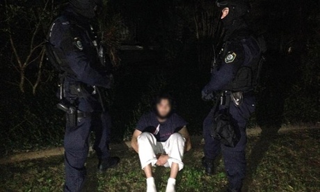 A suspect is guarded by police after the raids in Sydney. Photograph: /AAP/NSW Police