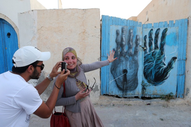 A Tunisian takes a photo of a mural by French artist Bom.K as part of the street art project 'Djerbahood'