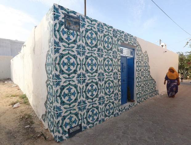 A Tunisian woman walks past a mural by Portuguese artist Diogo Machado, better known as Add Fuel, as part of the street art project 'Djerbahood'