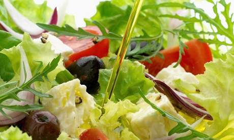 Olive oil pouring over greek salad in bowl