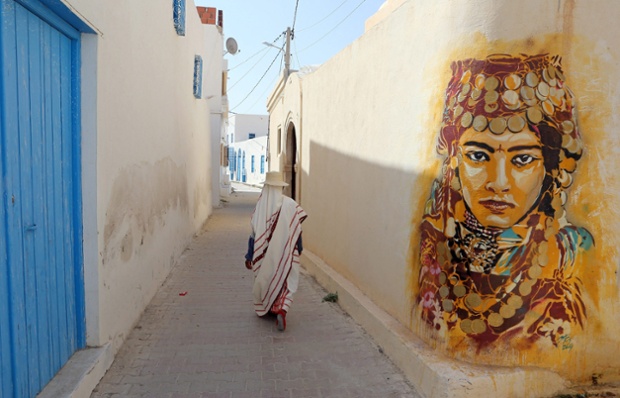A Tunisian woman walks past a mural by Spanish artist Btoy