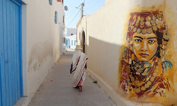 A Tunisian woman walks past a mural by Spanish artist Btoy as part of the street art project 'Djerbahood' in the village of Erriadh on the island of Djerba, Tunisia