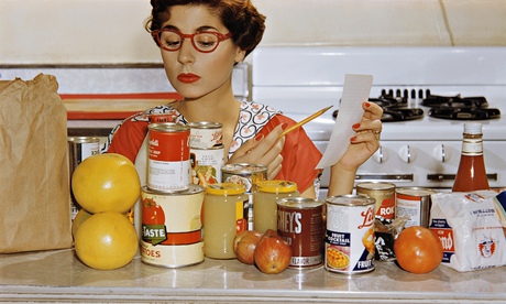 1960s woman in kitchen with glasses, shopping list and tins of food