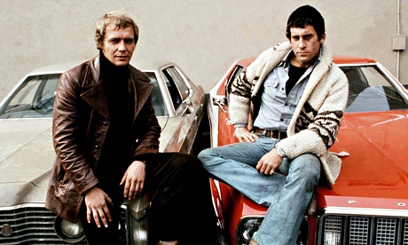 Starsky and Hutch sit on the bonnets of their cars, from the TV series of the 1970s