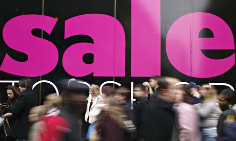 A big sale sign on a shop as customers rush past