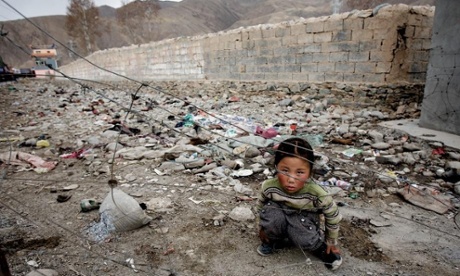 A girl squatting amid refuse and rubble in China.