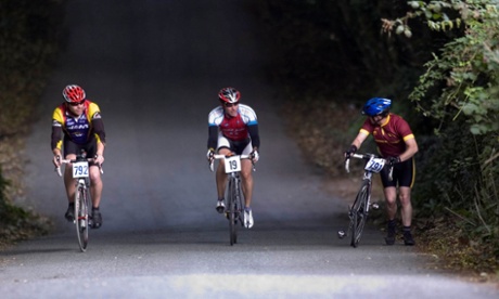 A cyclist pushes his bike up a hill as two others ride past 