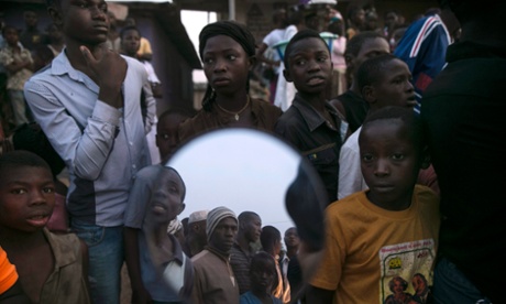 Bystanders, some reflected in a mirror, watch as the body of a suspected Ebola victim lies on a street in the town of Koidu, Kono district in Eastern Sierra Leone December 18, 2014.