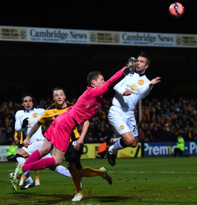 Chris Dunn of Cambridge United makes contact with Robin van Persie as he punches the ball clear.