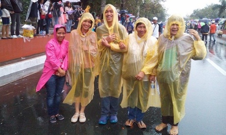 filipino family wearing yellow ponchos and waiting for pope francis in the rain in manila philippines