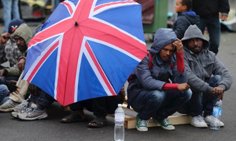Eritrean migrants take cover from the rain under an umbrella during the daily food distribution at the harbour in Calais, northern France, May 27, 2014.
