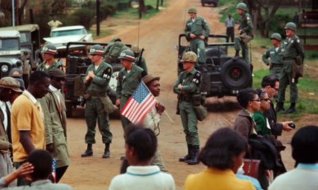 Stephen Somerstein, Man with American flag and marchers walking past federal troops guarding crossroads, 1965.